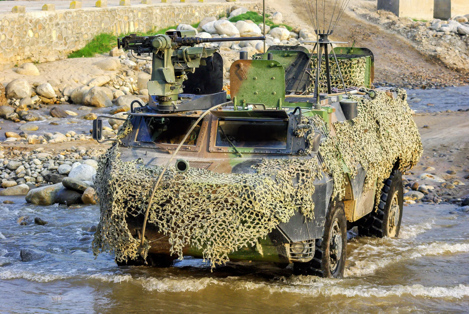 Véhicule blindé camouflé franchissant un cours d’eau lors d’un exercice militaire.
