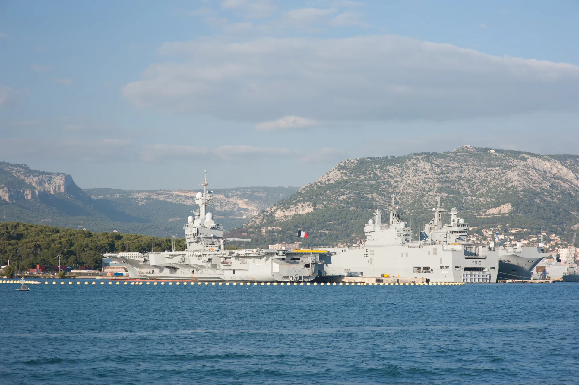 Navires militaires français amarrés dans une base navale, avec relief en arrière-plan.